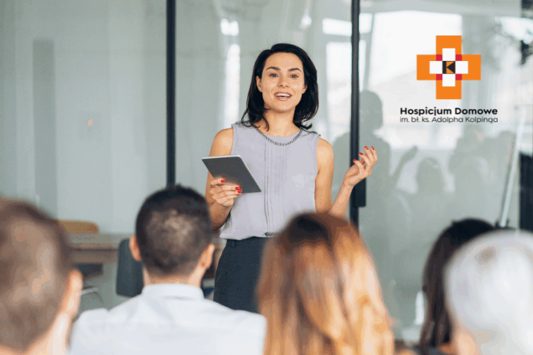 zdjecie przedstawiaj kobietę stojącą i przemawiającą do grupy osób siedzących na sali konferencyjnej.